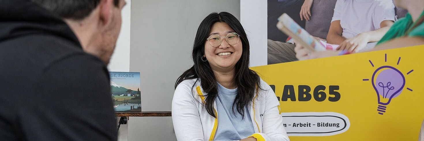 Eine Mitarbeiterin des LAB65 mit braunen Haaren, sitzt und lächelt.